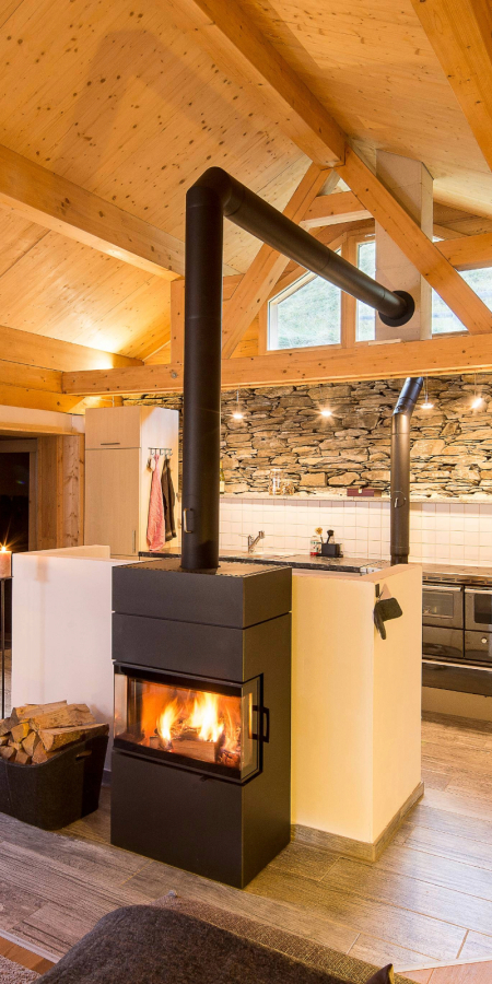 Gemütlicher Wohnraum mit Kamin und Blick in die Küche der Berghütte Pundelon