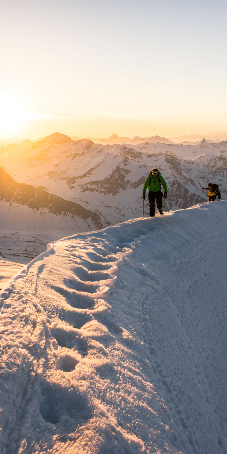 Zwei Skitourengänger auf einem verschneiten Gipfel im Moesano bei Sonnenaufgang (Foto: © Rudy Jörg)