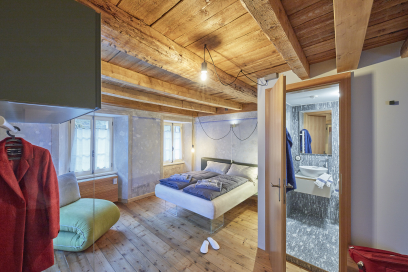 Charmantes Gästezimmer im BnB Ai Cav Calanca mit rustikalem Holzinterieur und moderner Ausstattung Gemütliches Schlafzimmer mit sichtbaren Holzbalken, Doppelbett und angrenzendem modernen Badezimmer in einem BnB