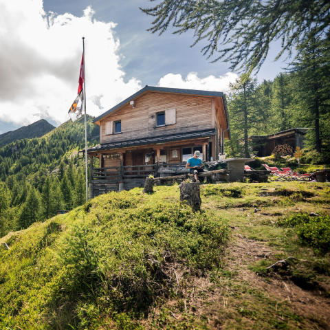 La Capanna Buffalora si trova in posizione idilliaca sopra la Val Calanca e offre relax immersi nella natura (Foto: © Marco Hartmann) Rifugio di montagna Capanna Buffalora con bandiera svizzera, circondato da boschi e montagne in posizione soleggiata