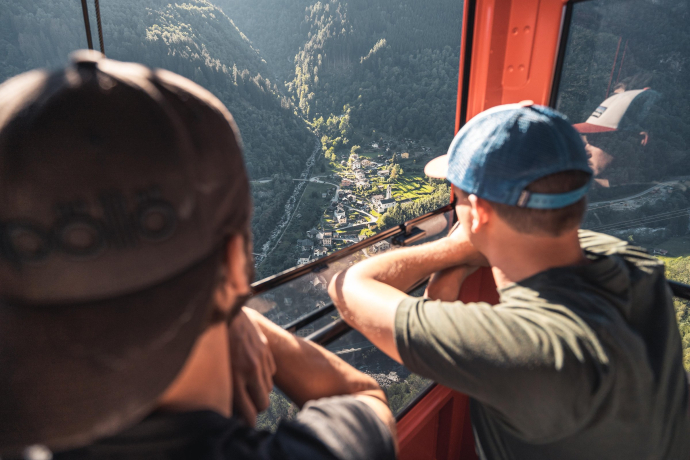 Fahrt mit der Seilbahn nach Braggio hoch über dem Calancatal (Foto: © Fabian Künzel) Zwei Männer blicken aus Seilbahn auf das Dorf Braggio