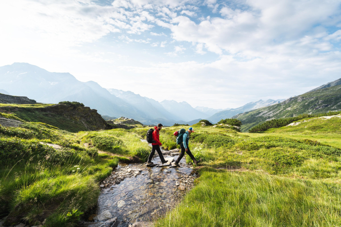Sul Sentiero Alpino Calanca: due escursionisti immersi nella natura alpina (Foto: © Thomas Vielgut) Due escursionisti attraversano un piccolo ruscello sul Sentiero Alpino Calanca, circondati dal paesaggio alpino