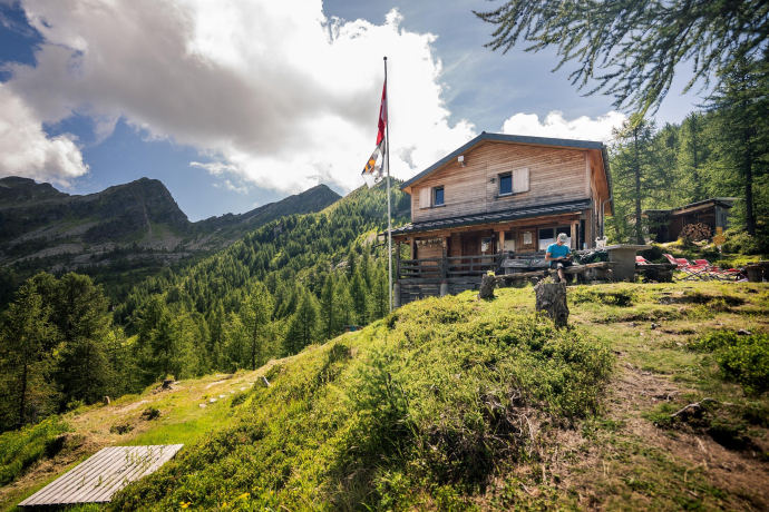 Rifugio di montagna Capanna Buffalora con bandiera svizzera, circondato da boschi e montagne in posizione soleggiata