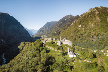 Ruderi del Castello di Mesocco su una collina boscosa con vista sulla valle alpina e le montagne circostanti