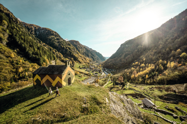 Wanderer vor der Kapelle Santa Maria Maddalena al Calvario im Calancatal mit Blick auf das herbstliche Tal