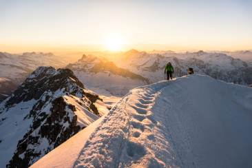 Zwei Skitourengänger auf einem verschneiten Gipfel im Moesano bei Sonnenaufgang (Foto: © Rudy Jörg)